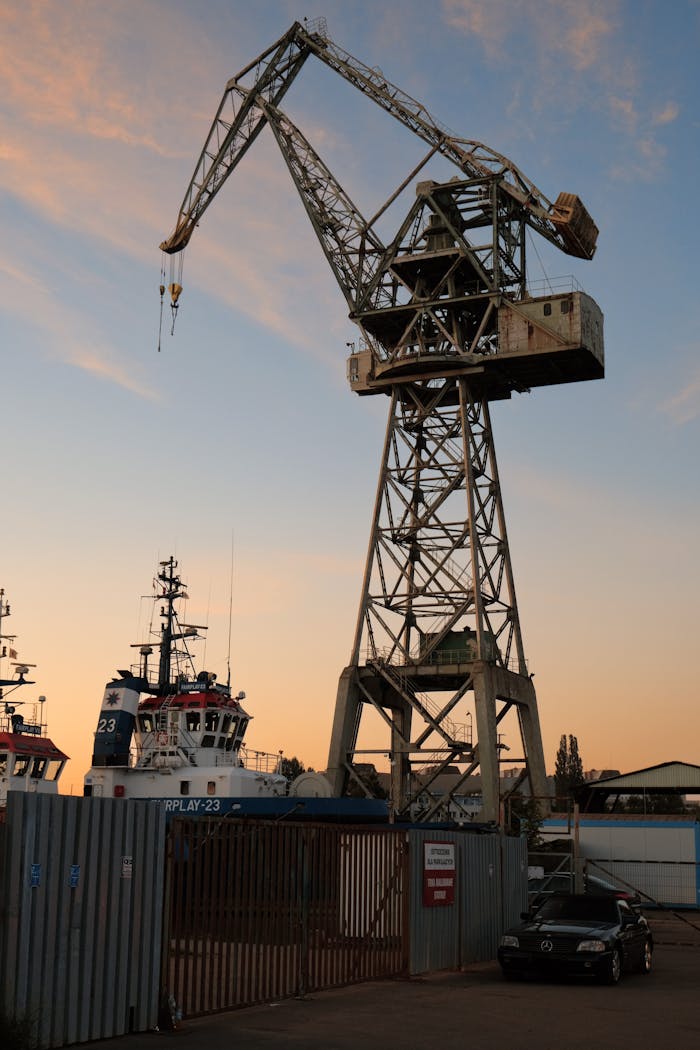 services-img-01 Large crane and ships in Gdańsk harbor at sunset, capturing an iconic industrial scene.